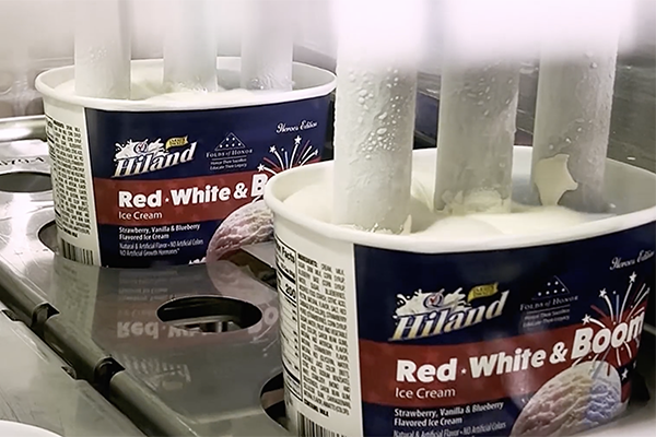 Hiland Red, White & Boom Ice Cream containers on a production line being filled from vertical nozzles dispensing ice cream.