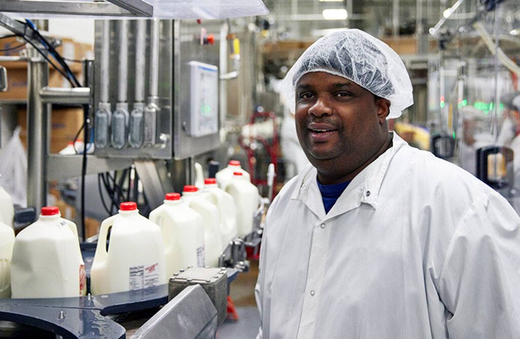 Hiland employee smiling standing in front of a conveyor belt loaded with jugs of milk
