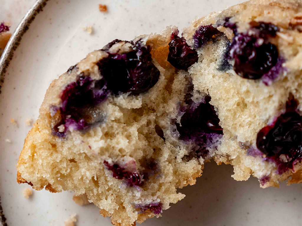 close up of a Blueberry Streusel Muffin cut in half featuring dark purple gooey blueberries