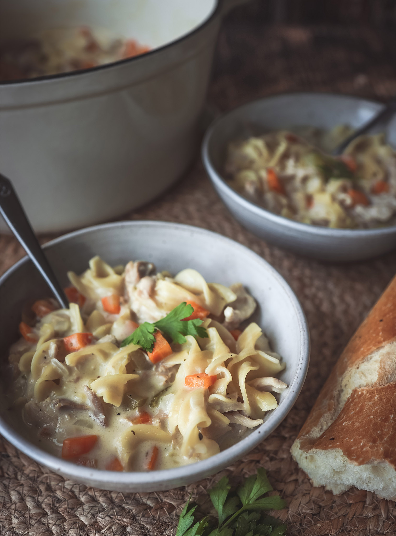 bowl of Creamy Chicken Noodle Soup with the serving cauldron out of focus in the background