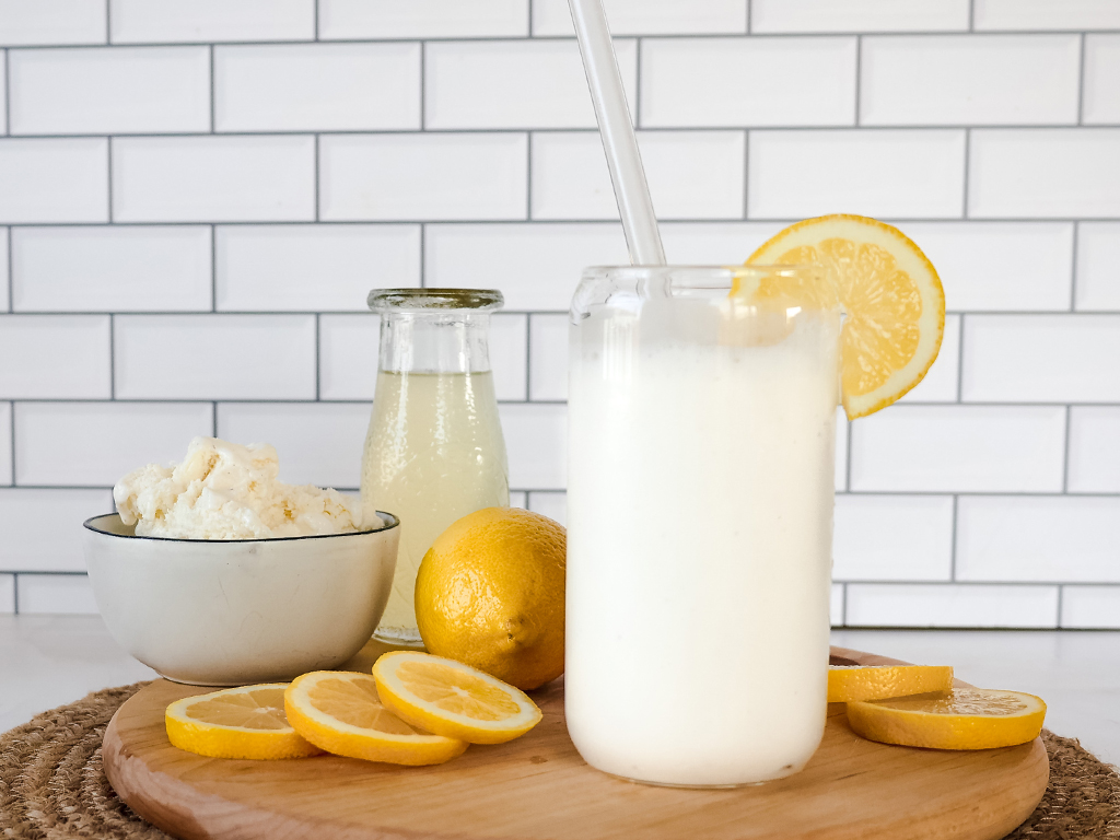 A refreshing glass of creamy lemonade garnished with a lemon slice, accompanied by a bowl of ice cream, a bottle of lemonade, and fresh lemon slices on a wooden board.