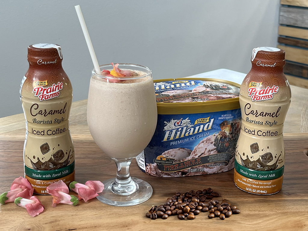 A caramel iced coffee shake served in a glass, surrounded by Prairie Farms Caramel Iced Coffee, Hiland Fire Hole Ice Cream, and coffee beans.