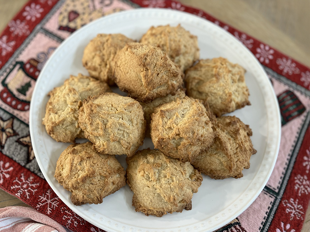 A plate of golden-brown eggnog cookies sits on a festive red and white holiday-themed tablecloth.