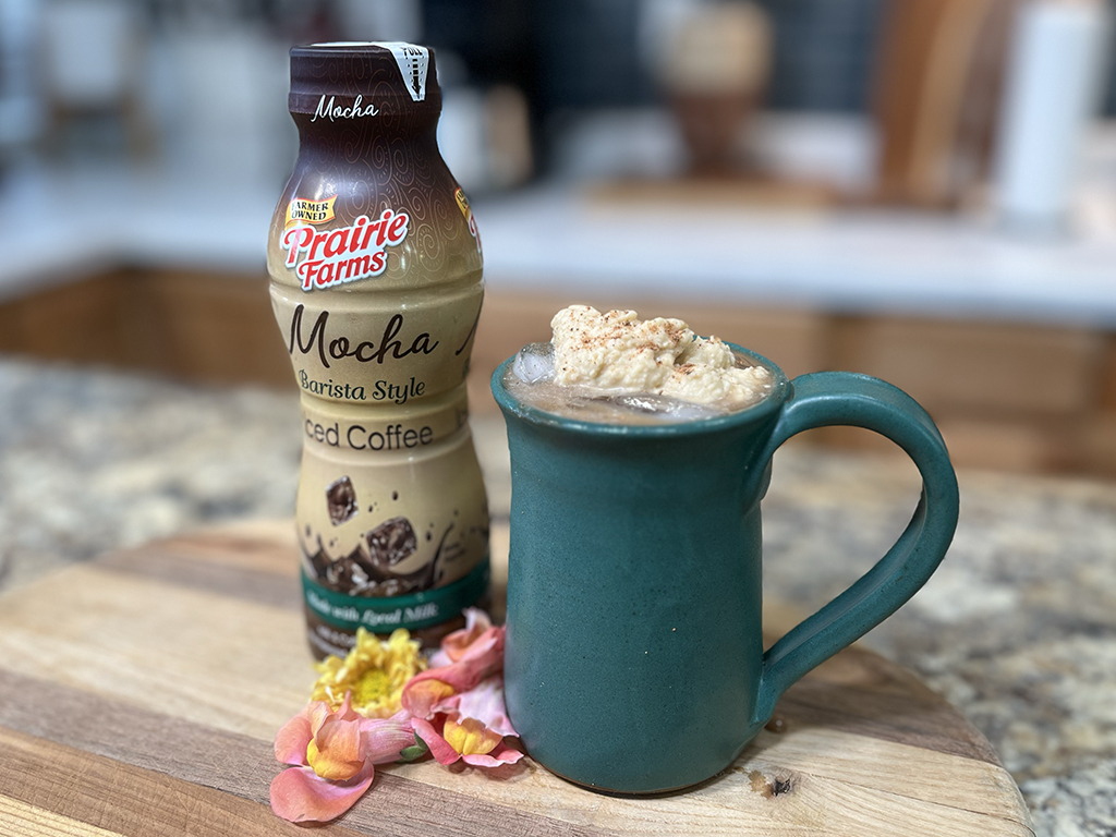 A creamy peanut butter mocha coffee shake served in a teal mug, paired with Prairie Farms Mocha Iced Coffee on a wooden surface.