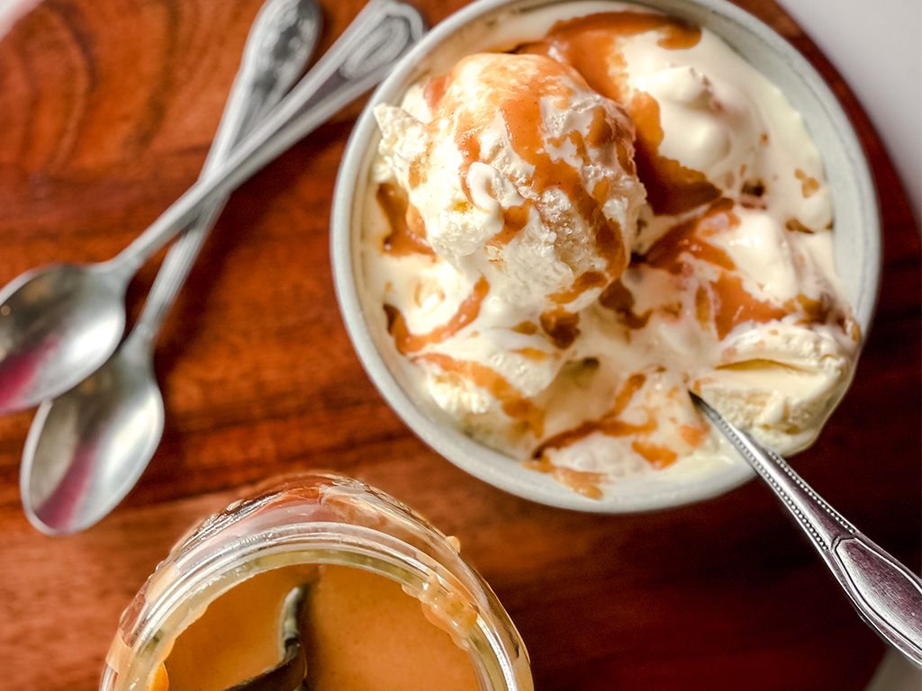 Overhead view of a bowl of vanilla ice cream drizzled with a creamy peanut butter topping, next to an open jar of the peanut butter topping.