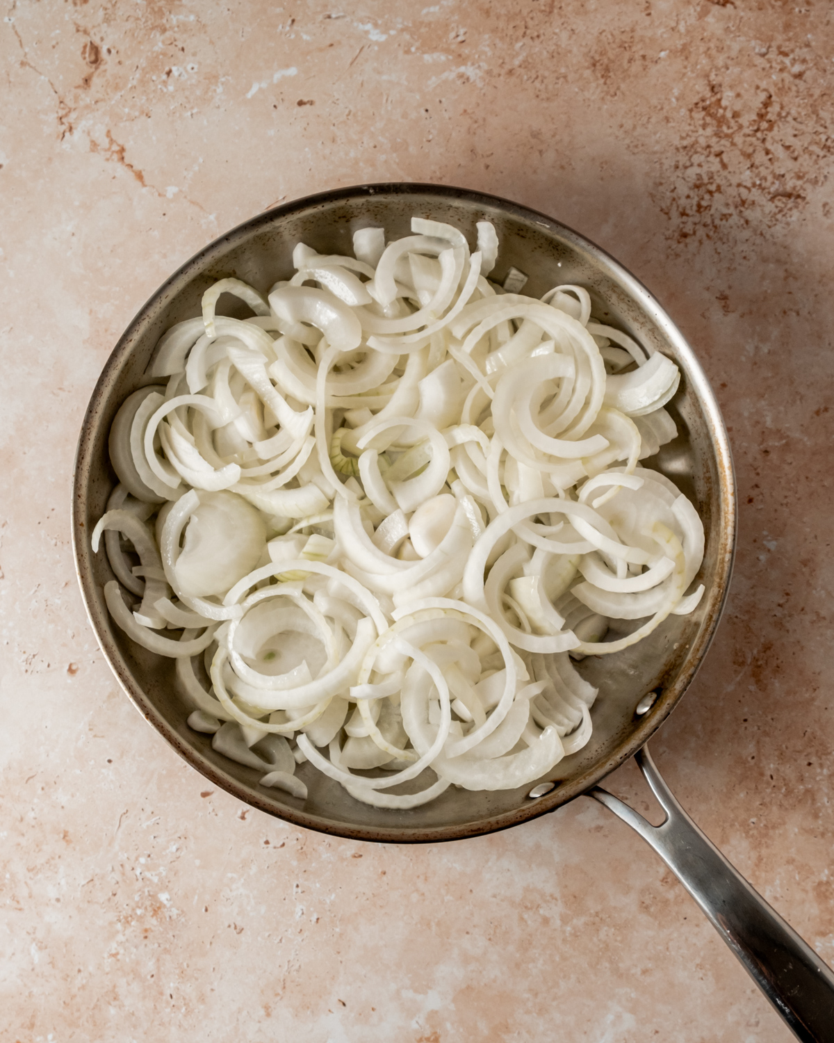 Raw sliced onions in a frying pan, ready for caramelizing.