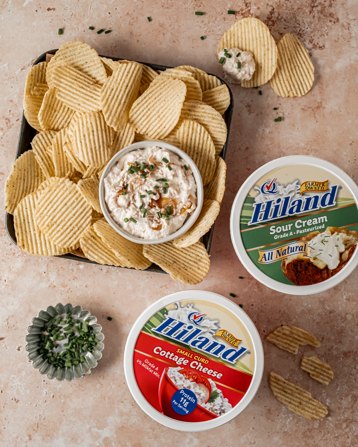 A tray of potato chips with a bowl of caramelized onion dip, next to containers of Hiland sour cream and cottage cheese.