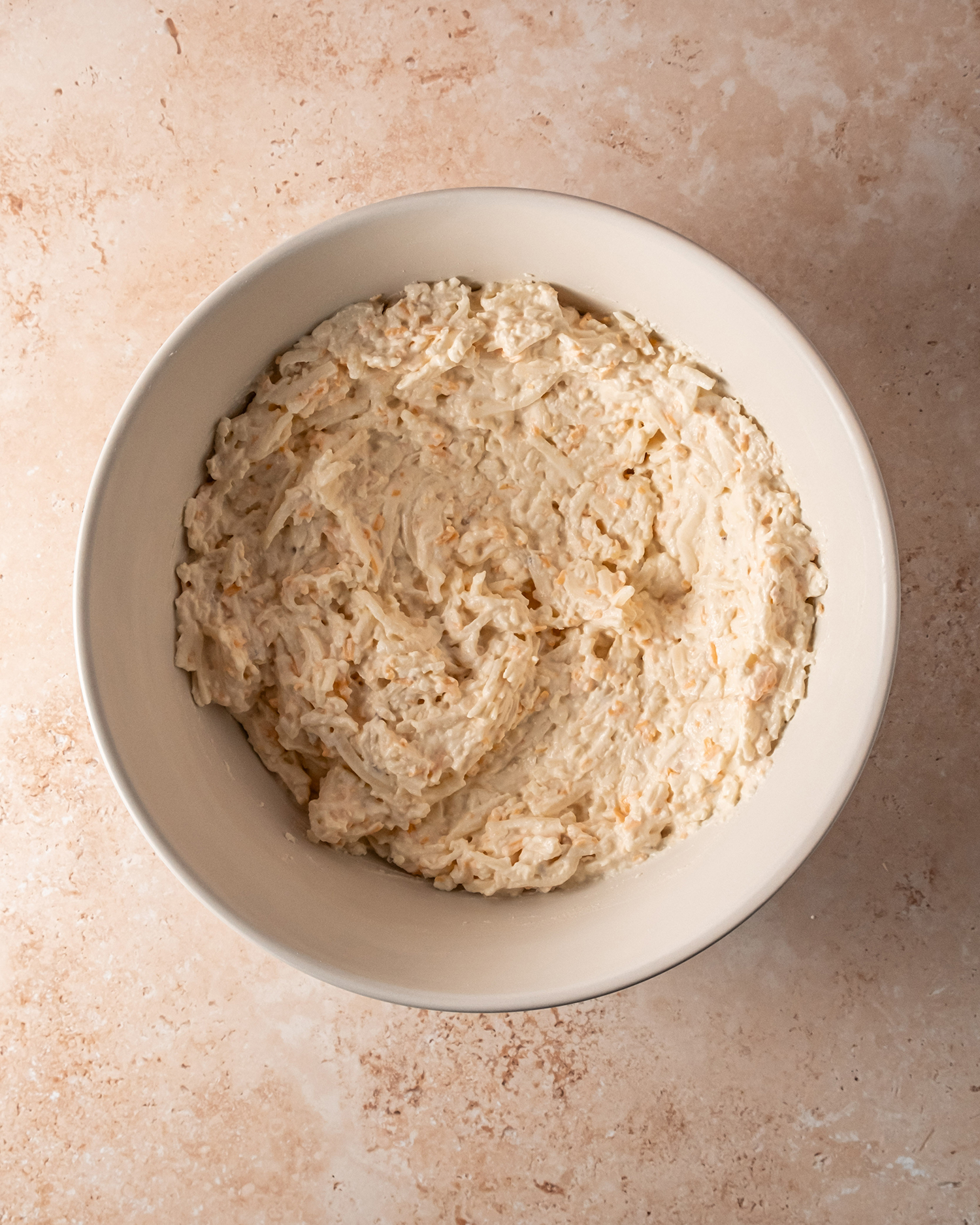 A bowl of creamy cheesy potato mixture prepared for baking, featuring a rich blend of shredded potatoes and cheeses.