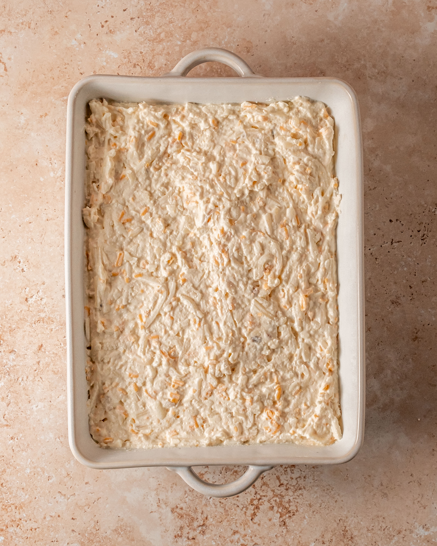 Cheesy potato casserole spread evenly in a baking dish, ready for the topping to be added before baking.