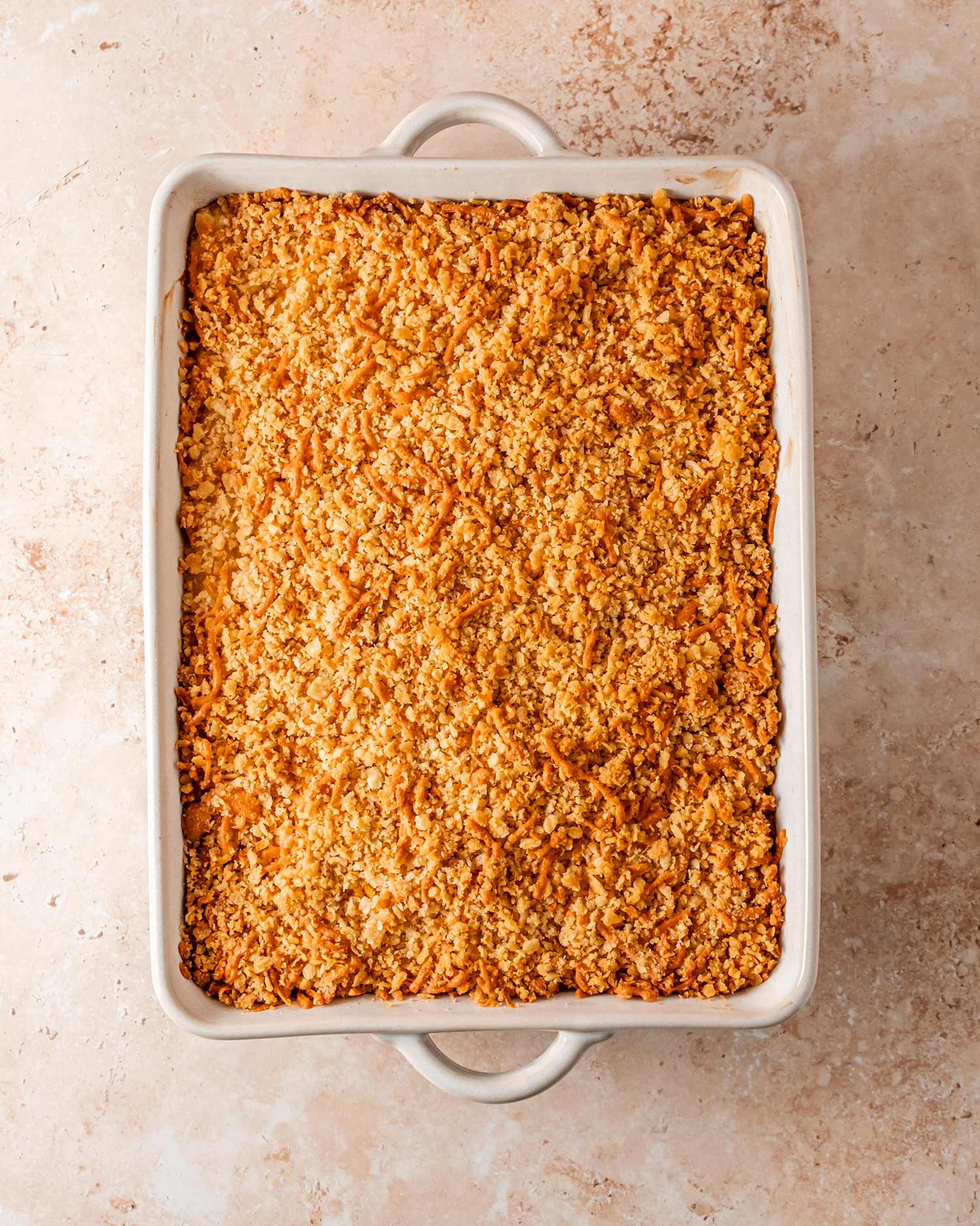 Golden cheesy potato casserole topped with a crispy breadcrumb and cheese layer, baked to perfection in a white dish.