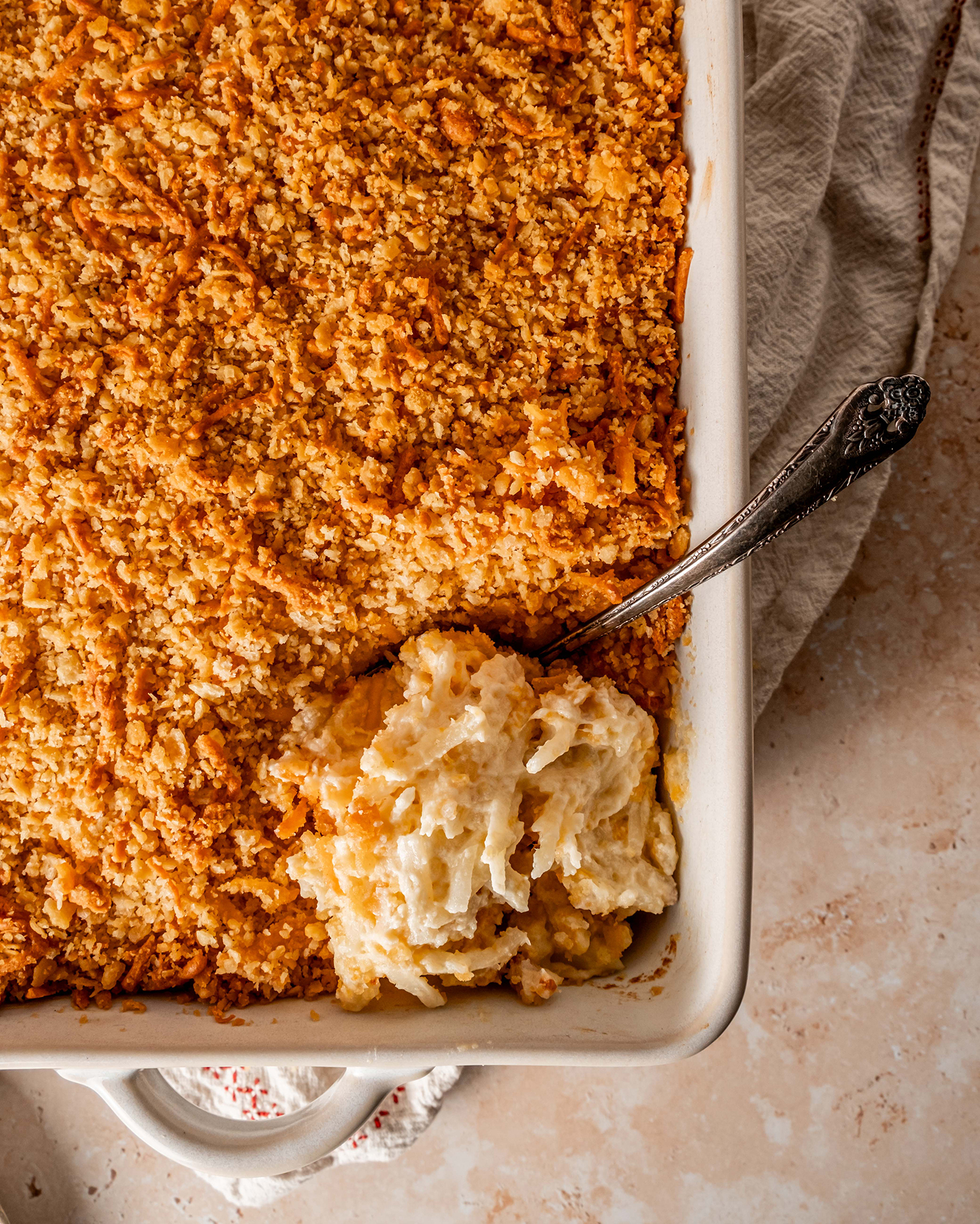 Golden cheesy potato casserole with a crispy breadcrumb topping, served with a scoop removed to reveal the creamy interior.