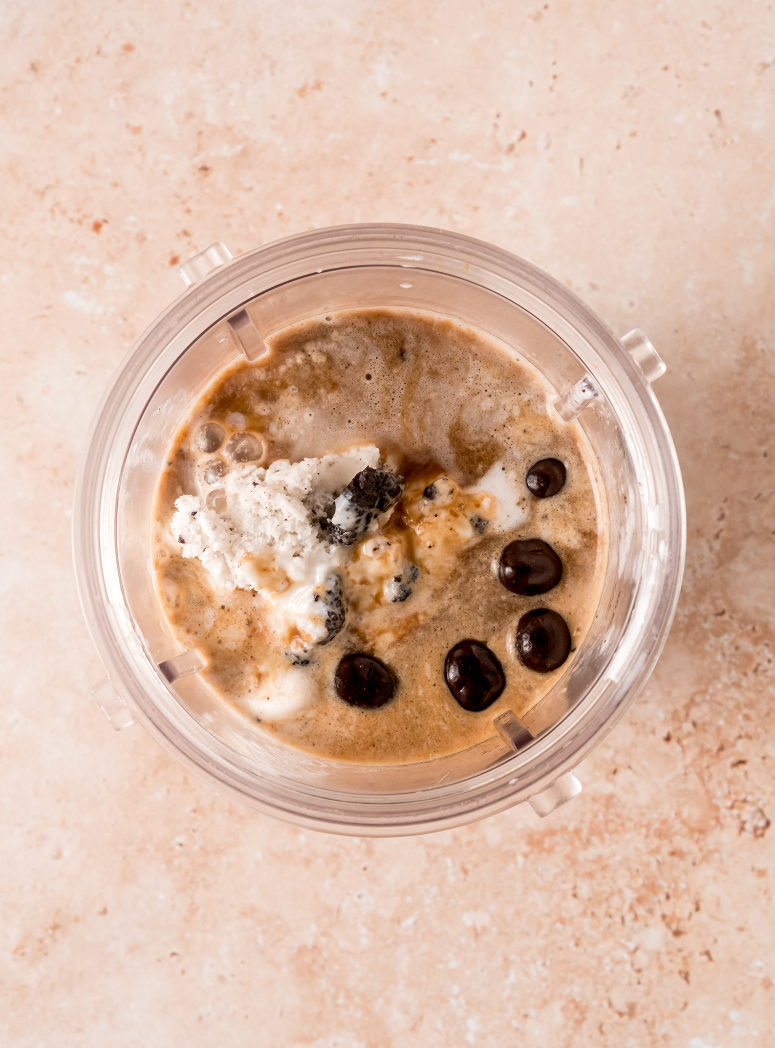 A close-up top view of a blender filled with Hiland Cookie Overload Light Ice Cream, espresso, and chocolate-covered espresso beans before blending.