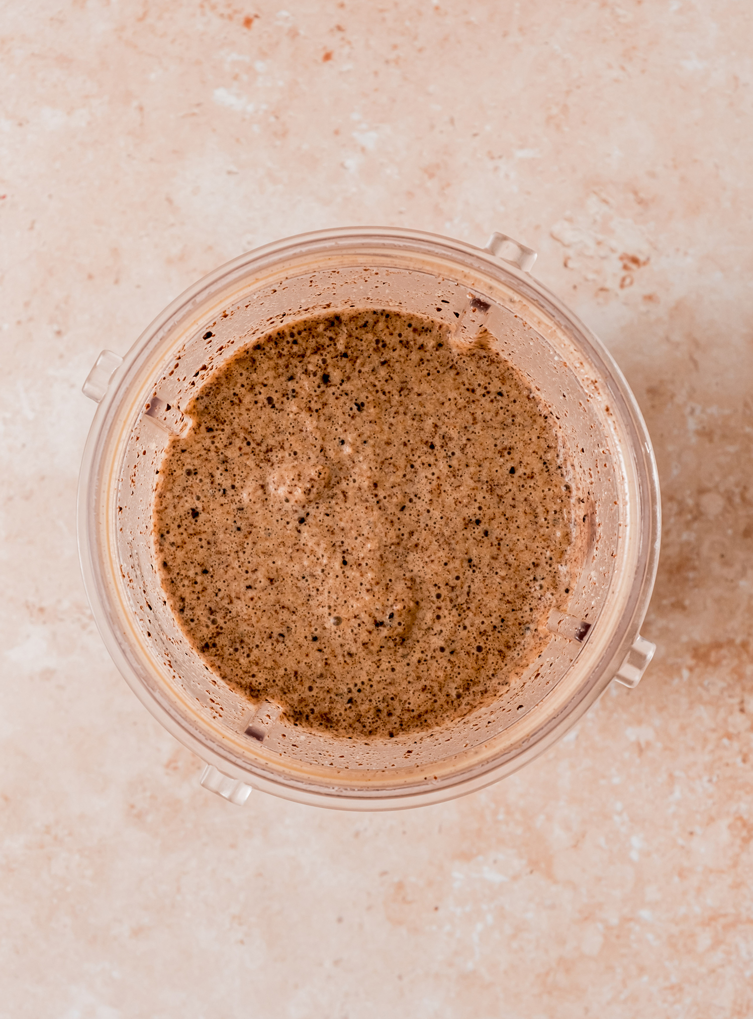 A top-down view of a blended cookies and cream mocha milkshake mixture in a blender cup, showing a creamy and speckled texture.