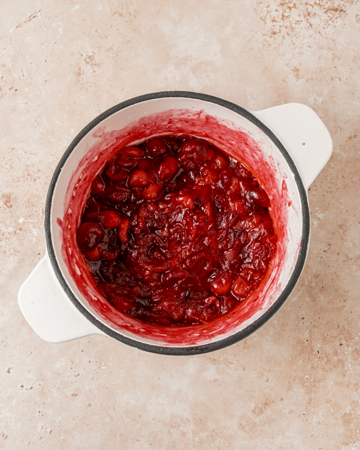 Cooked cranberries in a small saucepan, thickened and vibrant red, ready to be used in the cheesecake filling.