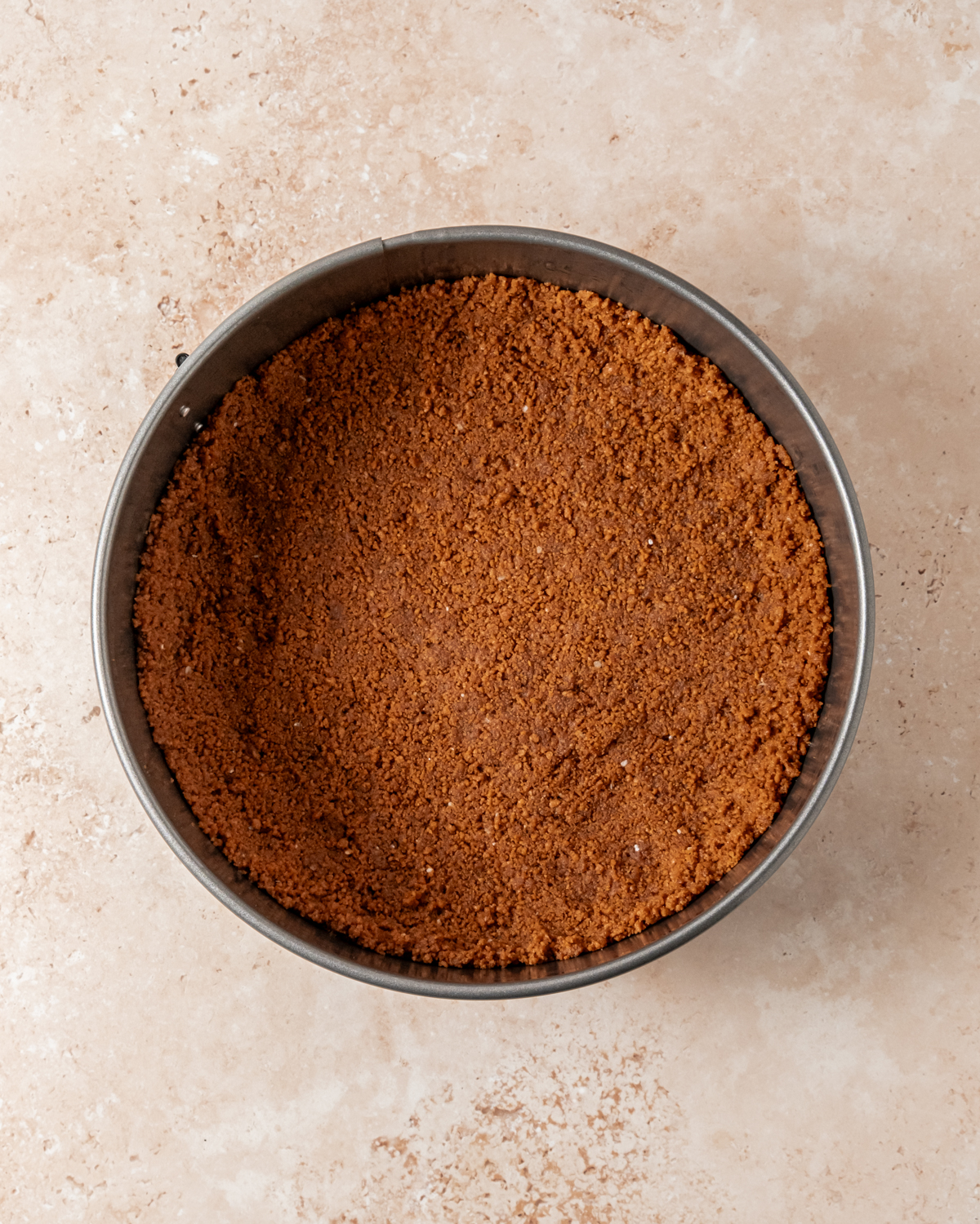 Prepared graham cracker crust pressed firmly into the base of a springform pan, ready to hold the cheesecake filling. The crust appears evenly packed and slightly golden brown.