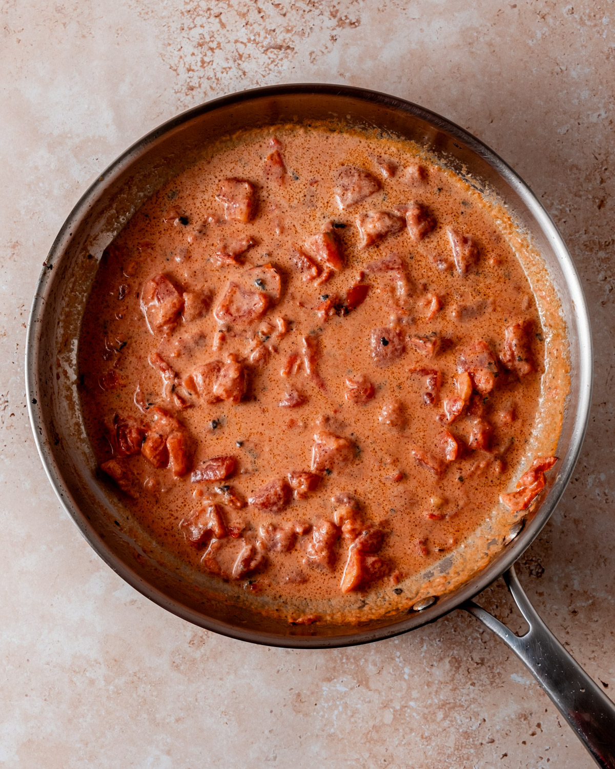 A creamy tomato-based sauce simmers in a skillet with visible chunks of tomatoes and spices.