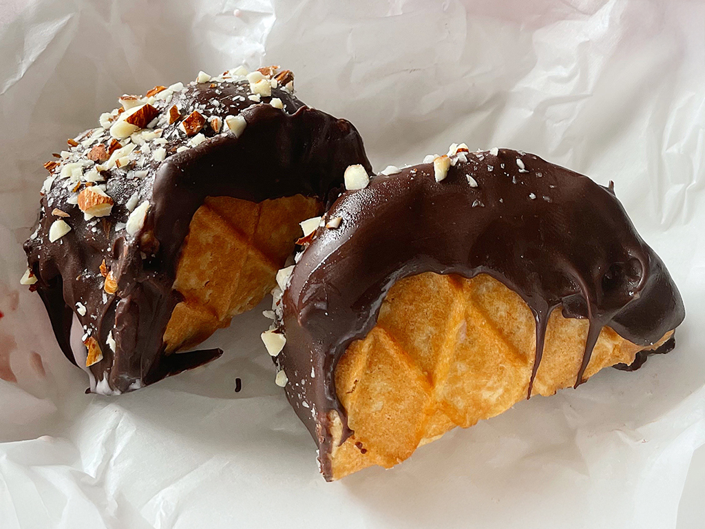 Mini choco tacos with waffle shells filled with ice cream, dipped in chocolate and topped with chopped nuts.