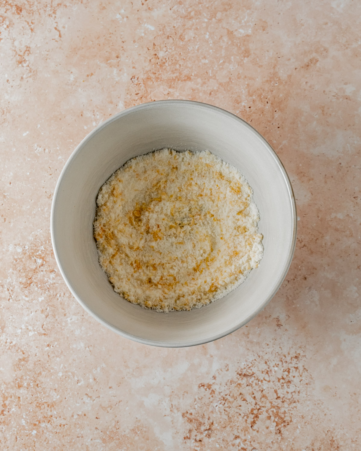 Bowl filled with crumbly flour mixture for orange shortbread cookies, with visible zest speckled throughout, set on a neutral countertop.