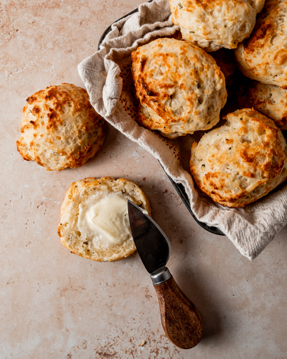 Warm, flaky parmesan rosemary drop biscuit split open and buttered, displayed with a basket of freshly baked biscuits.