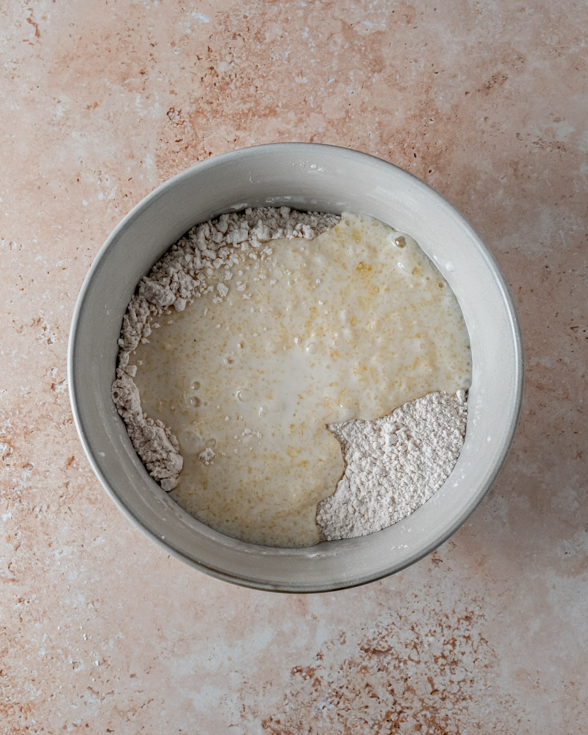 A mixing bowl combining dry ingredients, buttermilk, and butter for Parmesan rosemary biscuit dough, with a rustic texture.