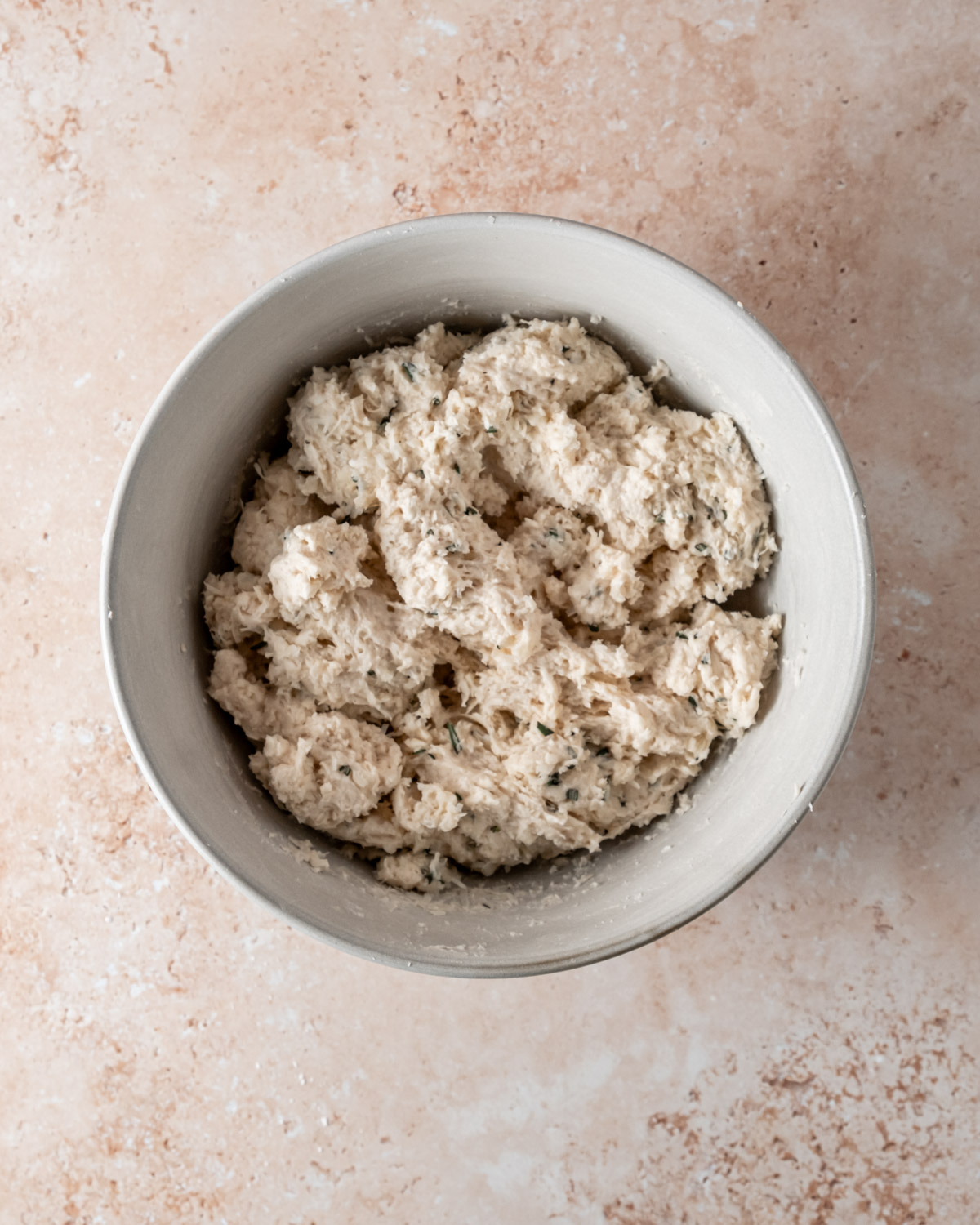 A bowl of Parmesan rosemary biscuit dough ready for baking, showcasing flecks of fresh herbs for added flavor.