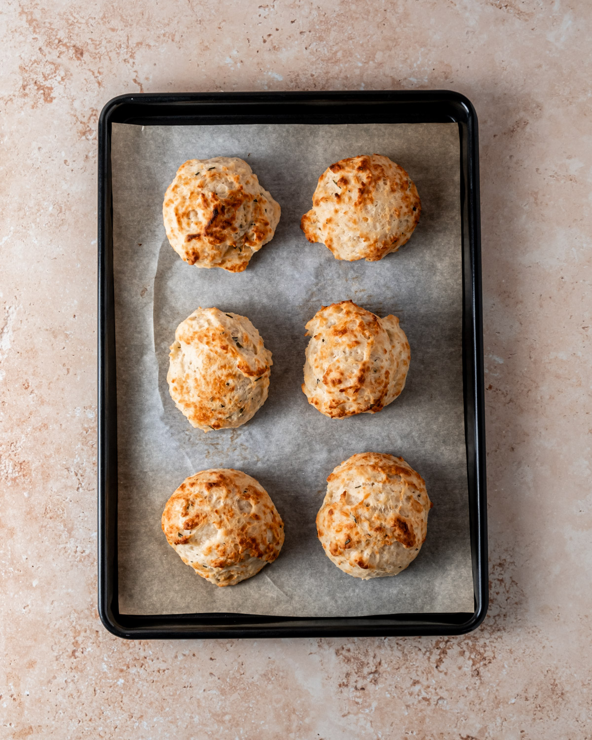 Freshly baked Parmesan rosemary biscuits with golden tops, cooling on a parchment-lined baking sheet.