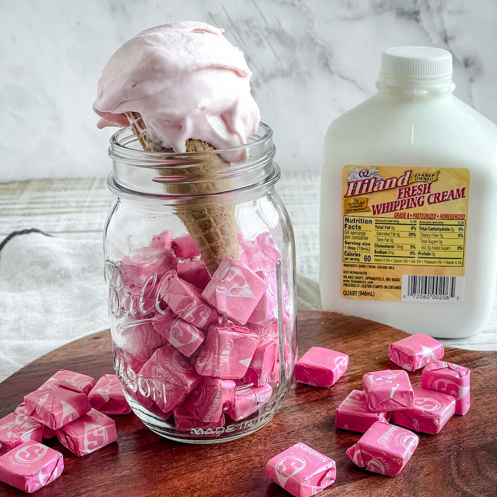 pink taffy ice cream in a cone, inside a glass jar, container of cream in background