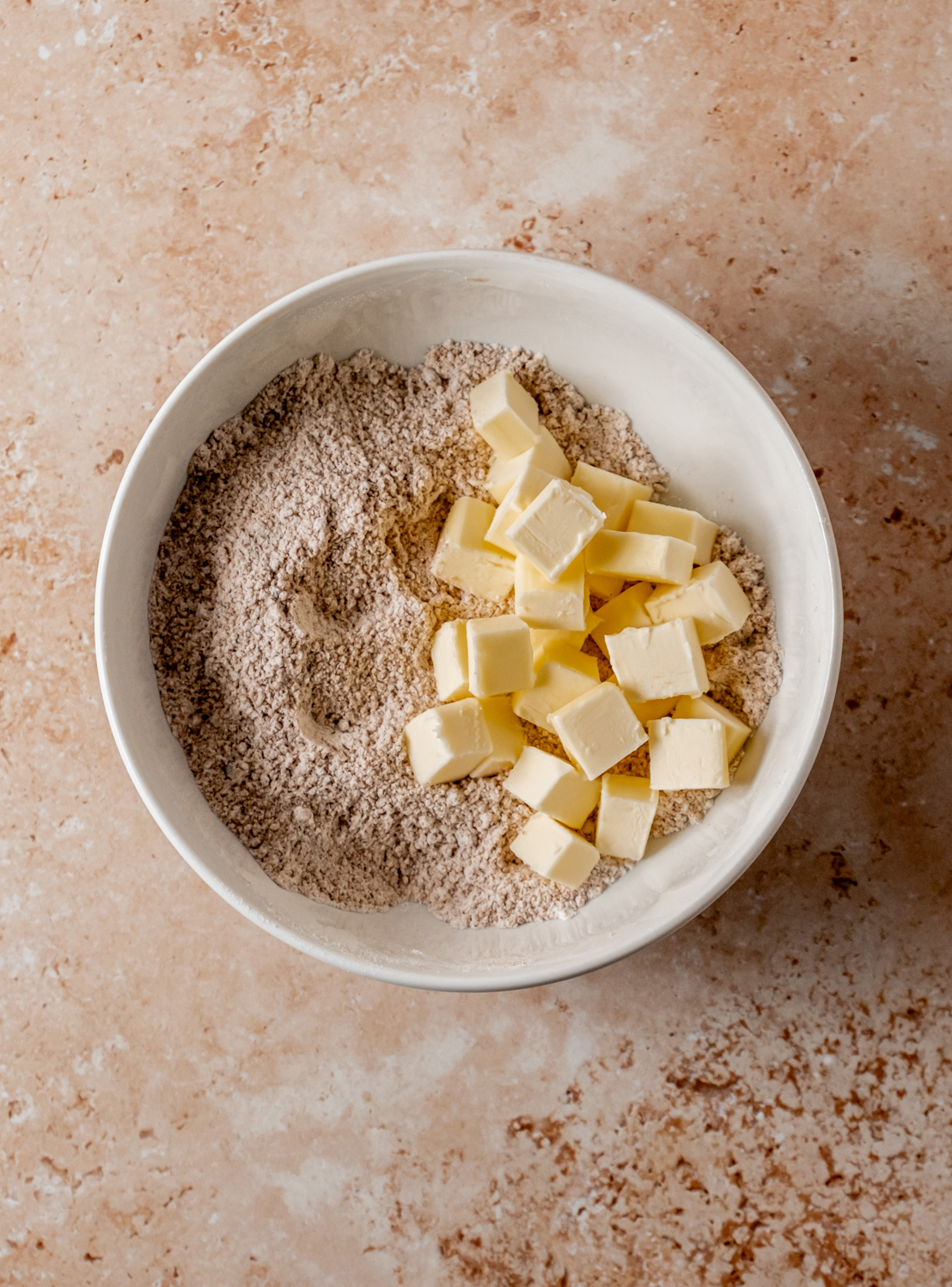 A bowl of flour and cubed butter ready to be mixed on a light stone countertop.