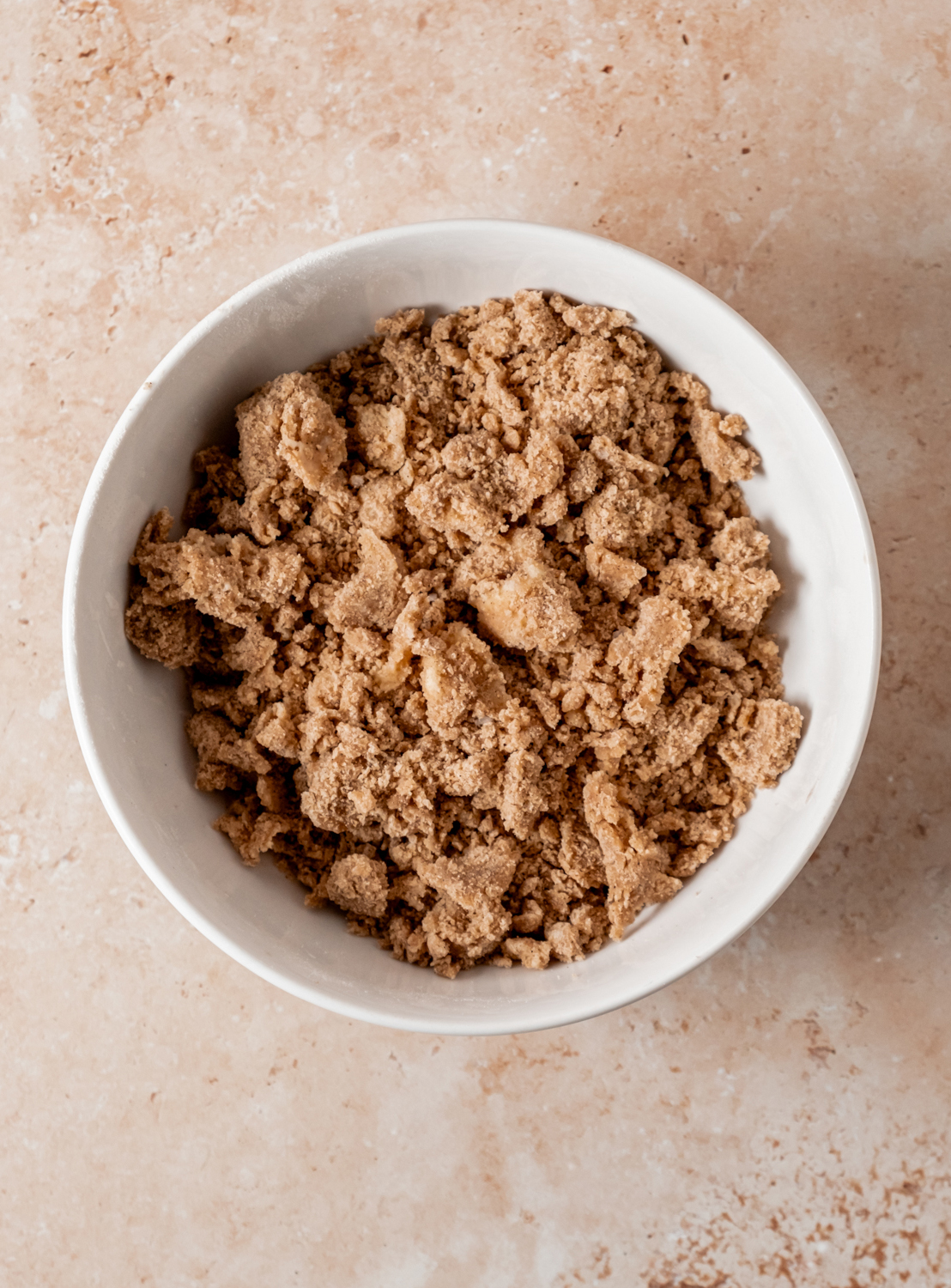 A bowl of prepared streusel topping with crumbly texture on a light stone countertop.