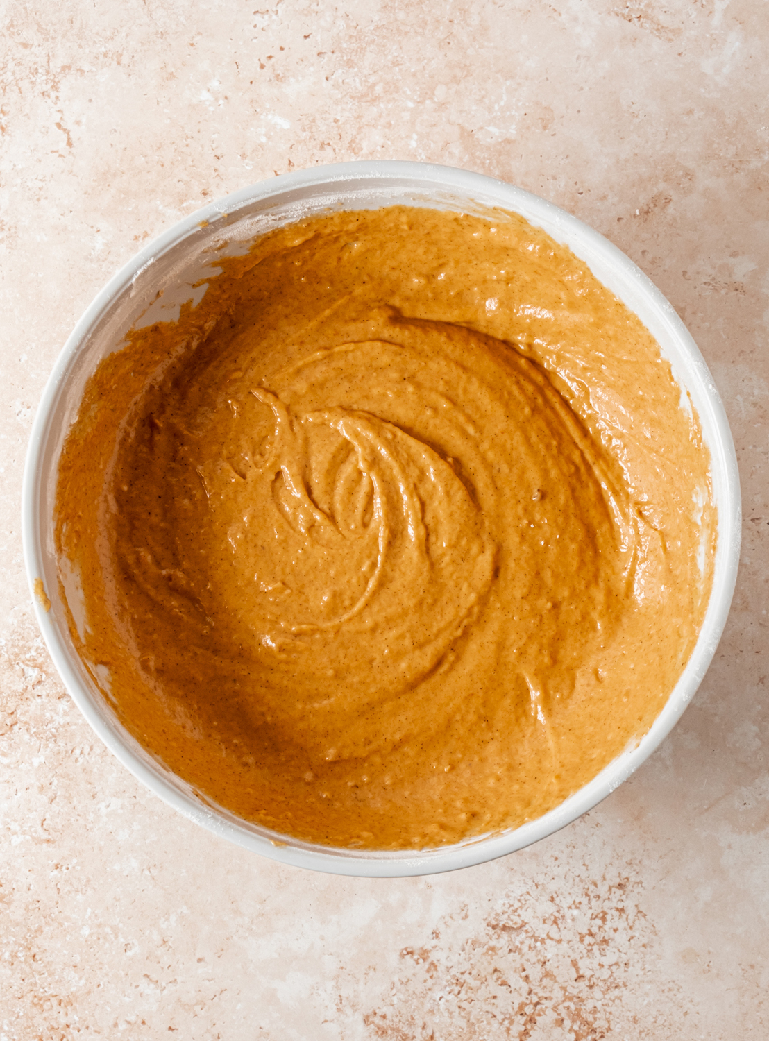 A bowl of smooth pumpkin batter ready for baking on a light stone countertop.