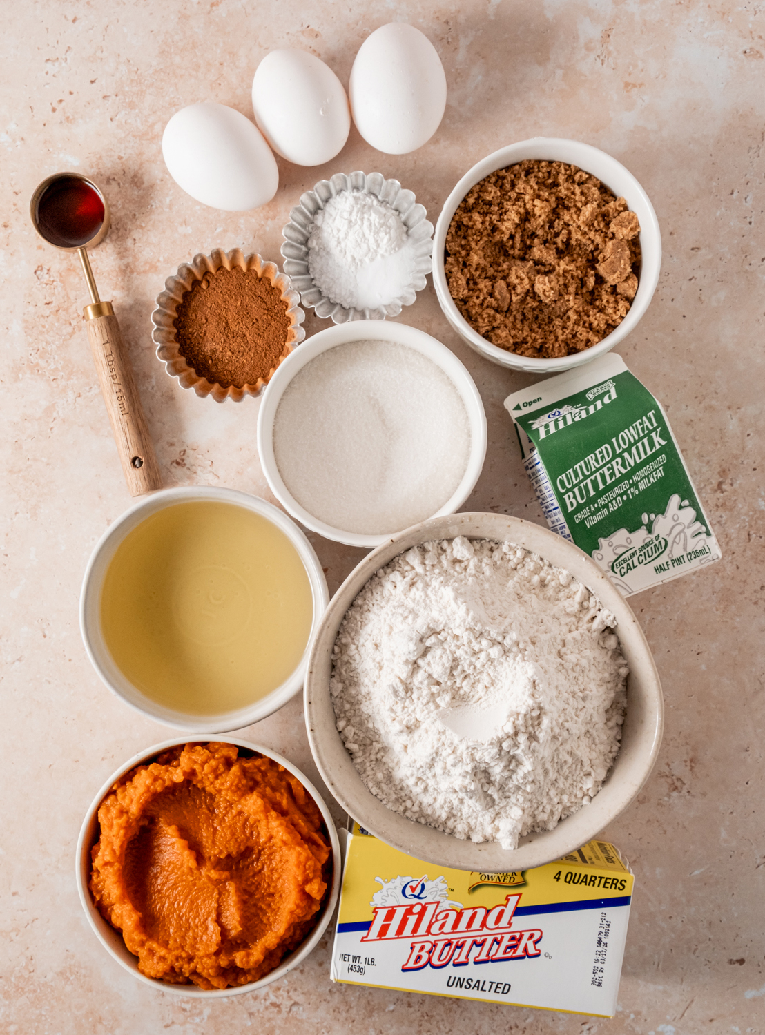 An assortment of ingredients for pumpkin streusel muffins, including eggs, sugar, flour, pumpkin puree, Hiland butter, and buttermilk.