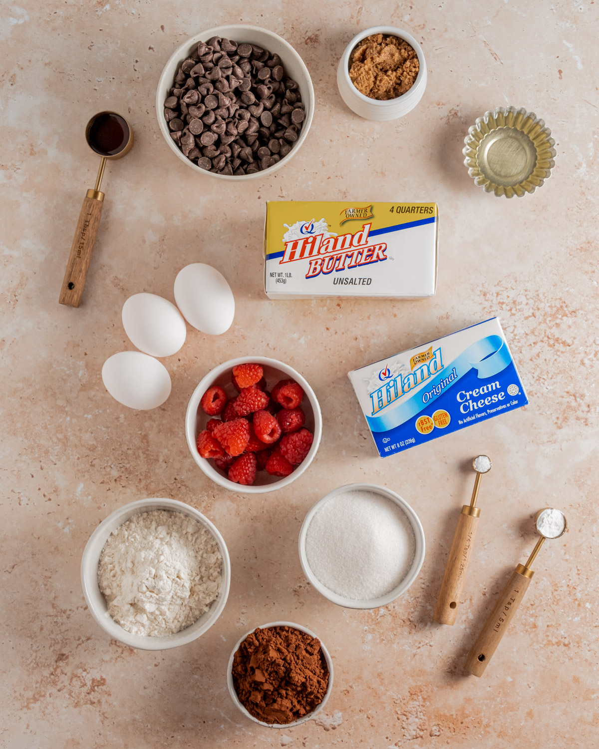 Ingredients for raspberry cheesecake brownies, including Hiland Butter, Hiland Cream Cheese, chocolate chips, fresh raspberries, and baking supplies.