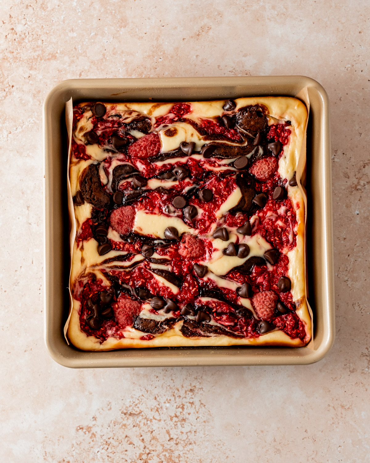 Freshly baked raspberry cheesecake brownies in a pan, swirled with cheesecake, chocolate, and raspberry toppings.