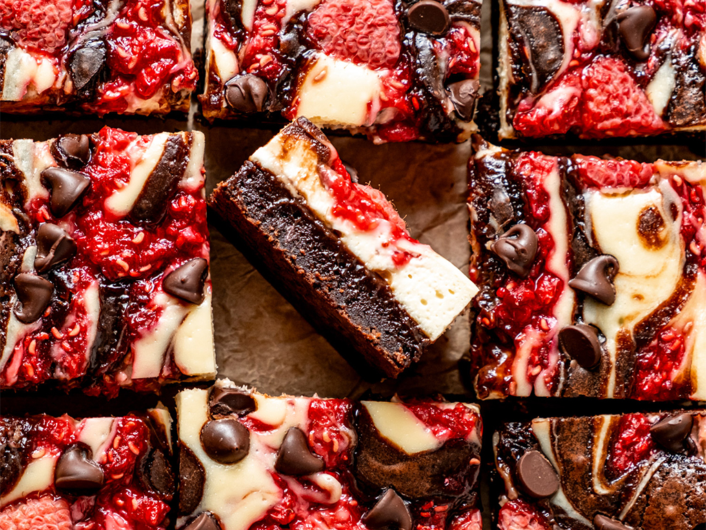 Close-up of raspberry cheesecake brownies with layers of chocolate brownie, creamy cheesecake, fresh raspberries, and chocolate chips.