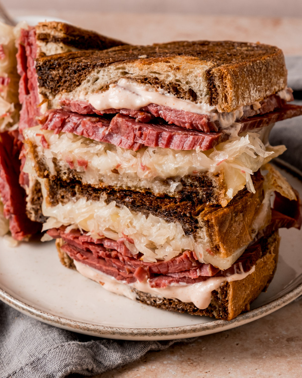 A close-up of a stacked Reuben sandwich with layers of corned beef, sauerkraut, melted Swiss cheese, and homemade Russian dressing between slices of toasted rye bread. The dressing drips slightly from the edges.