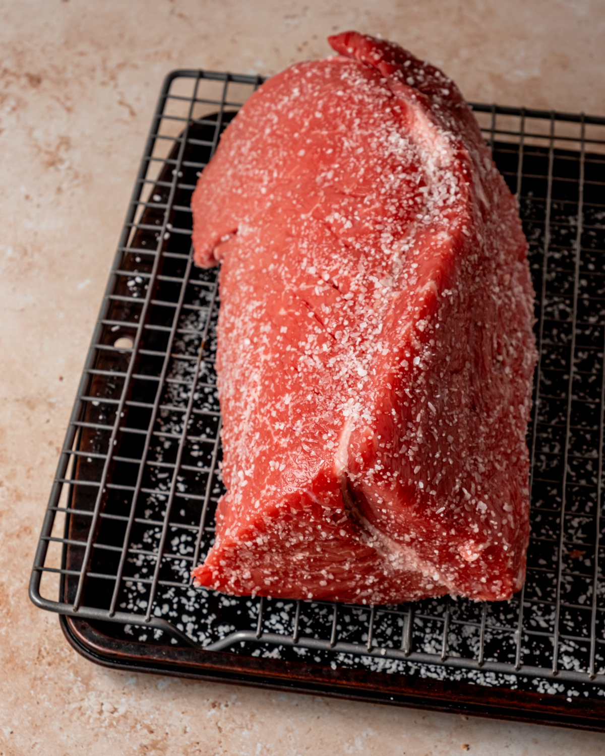 A large salted roast beef cut resting on a wire rack over a baking sheet, ready for roasting.