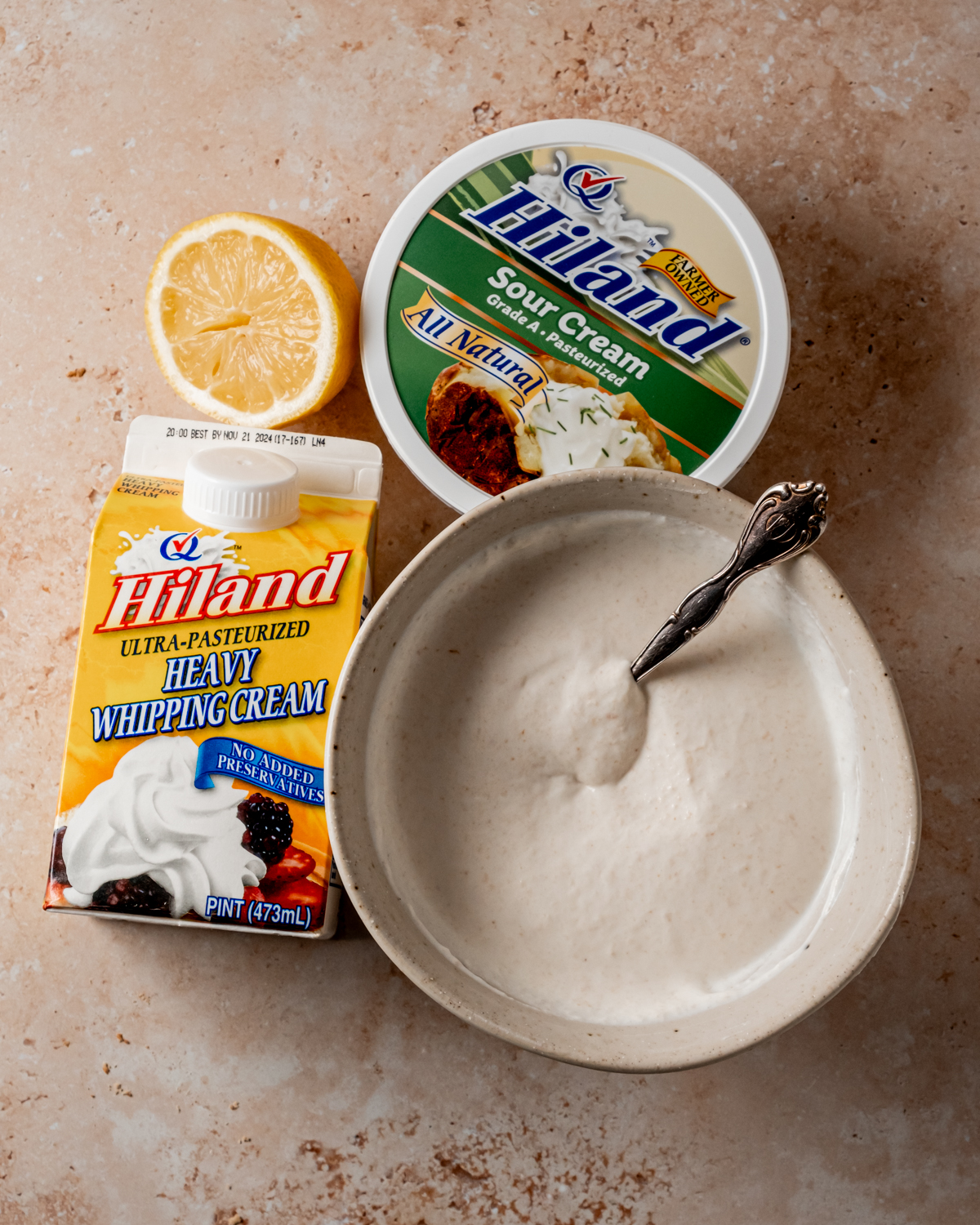 A bowl of creamy sauce made with Hiland sour cream and heavy whipping cream, next to a lemon and their respective packaging.