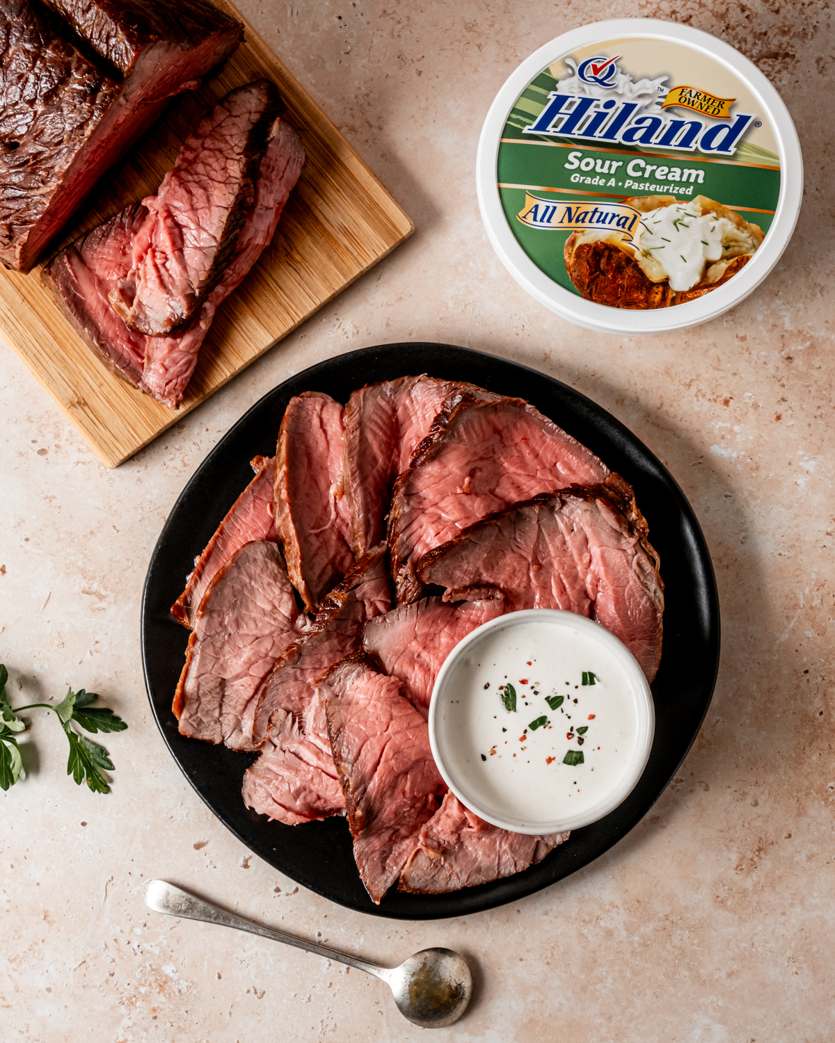 Slices of roast beef with creamy sauce, with a Hiland sour cream container and additional roast beef slices on a wooden board.