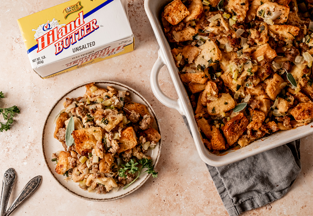 A serving of sausage and sage stuffing on a plate next to a box of Hiland butter, showcasing the final dish alongside the key ingredients.