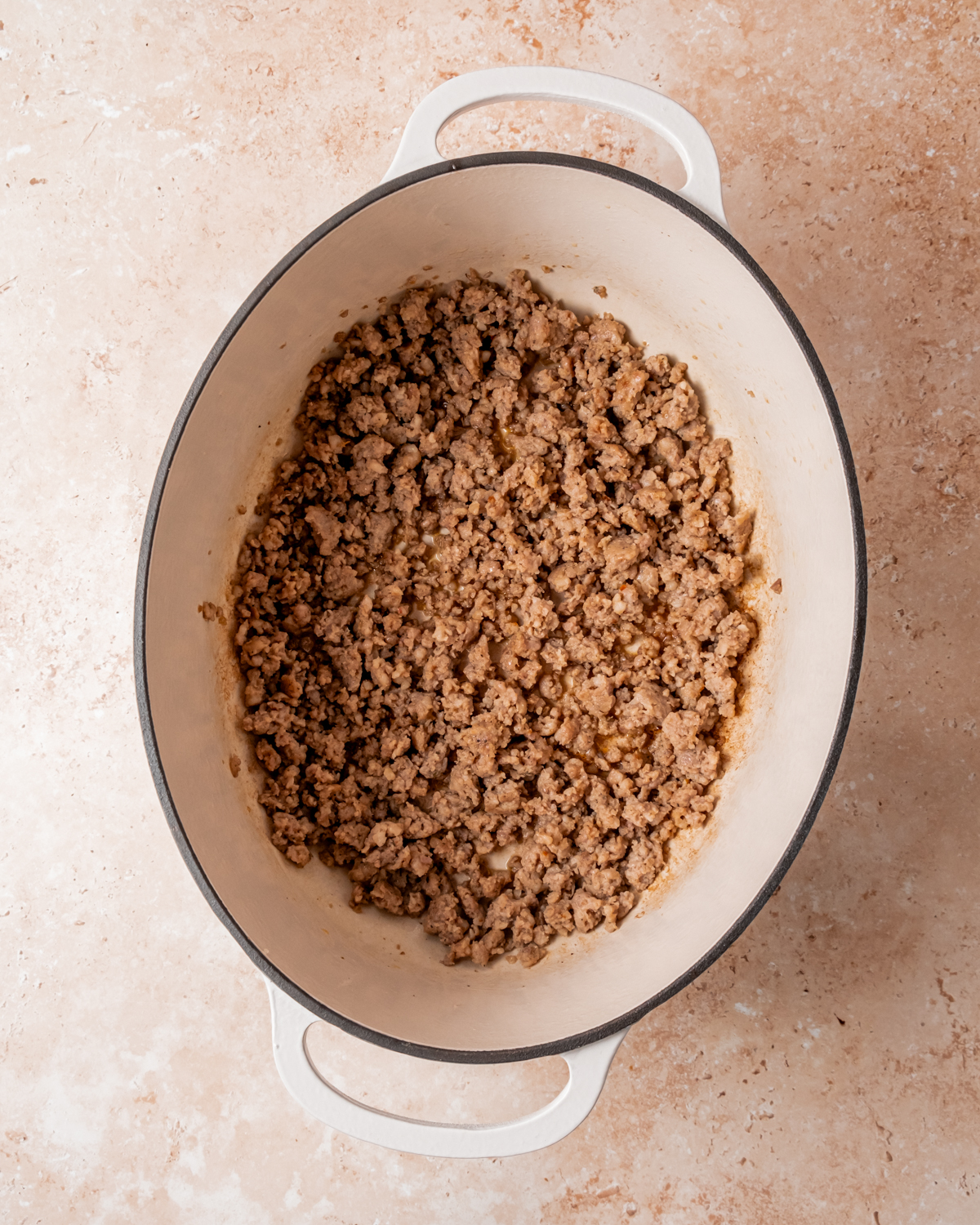 Cooked ground sausage in a large white pot, showing a browned and crumbly texture for use in stuffing preparation.