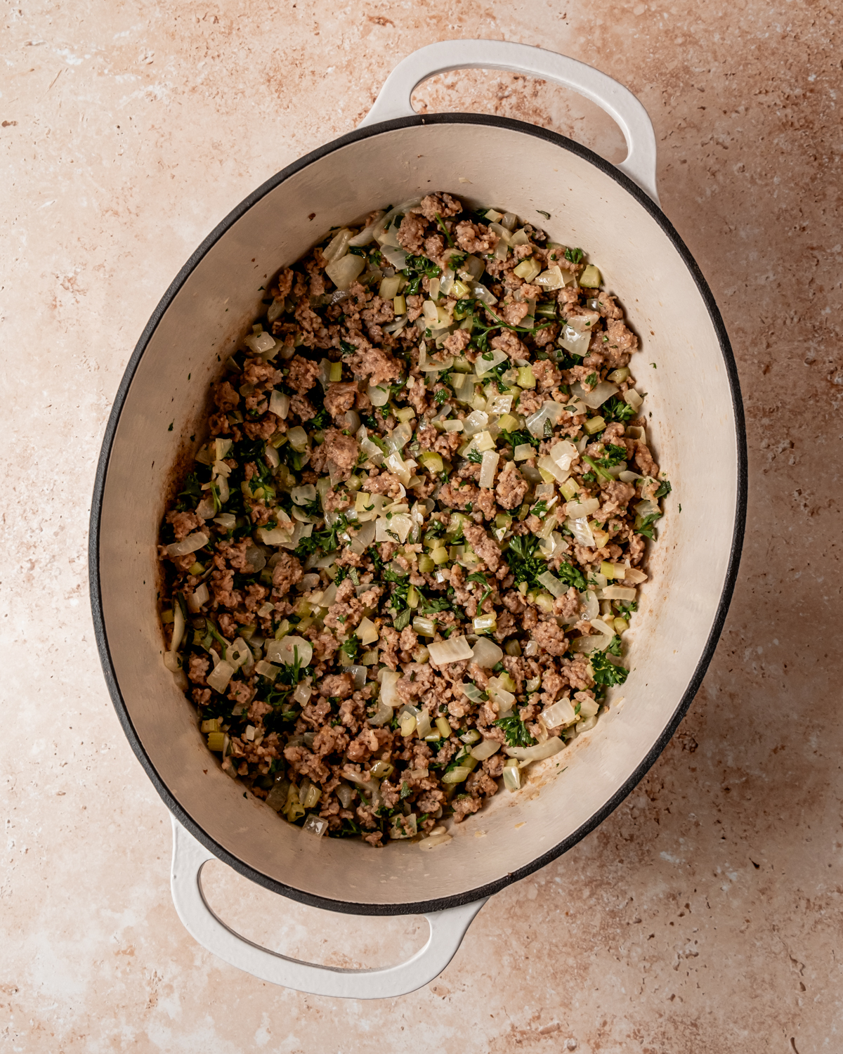 The cooked sausage mixed with sautéed onions, celery, and fresh parsley in the white pot, creating the savory base for the stuffing.