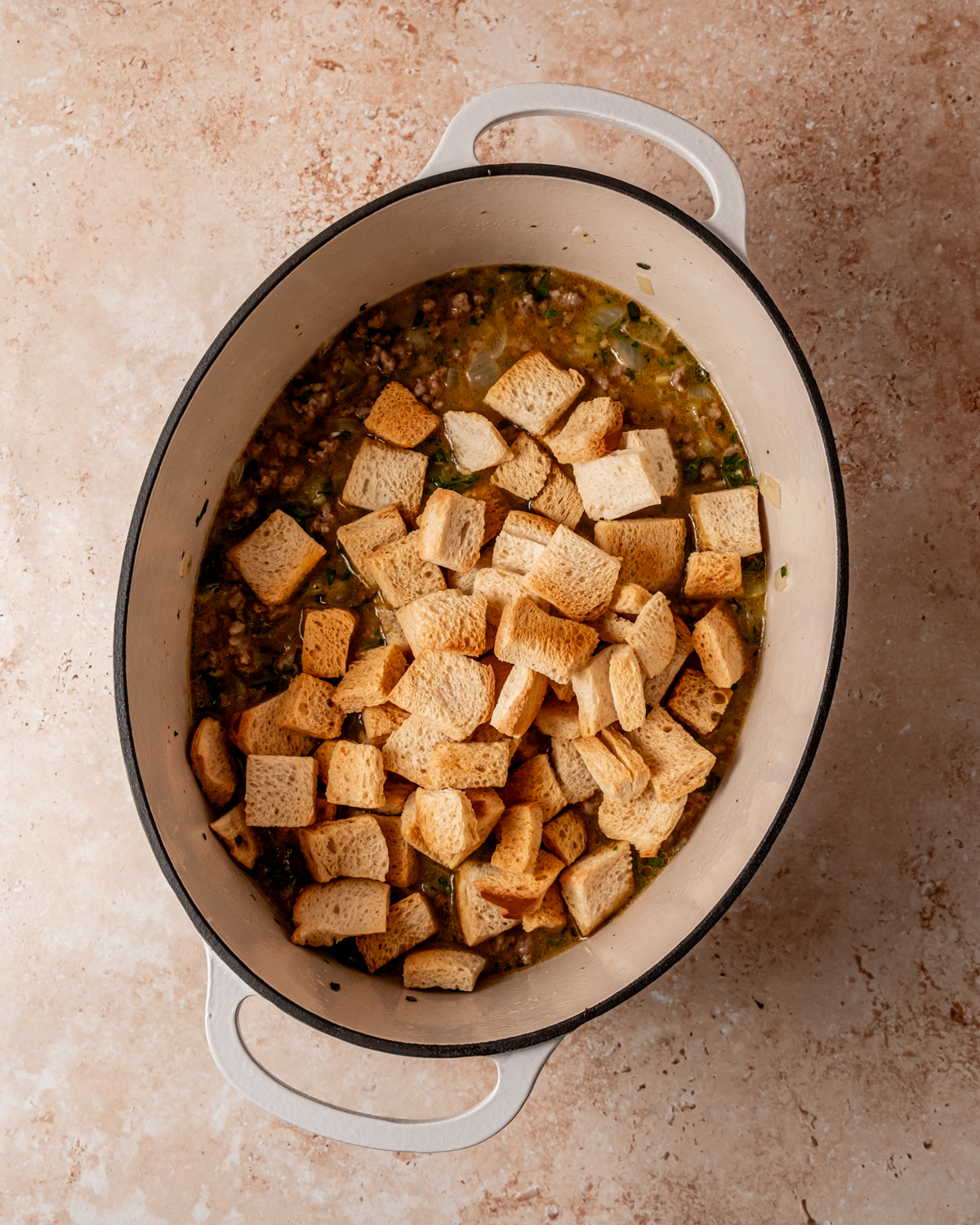 Cubed bread added to the mixture of sausage, onions, and celery in the pot, soaking up the flavors as it combines for the stuffing dish.