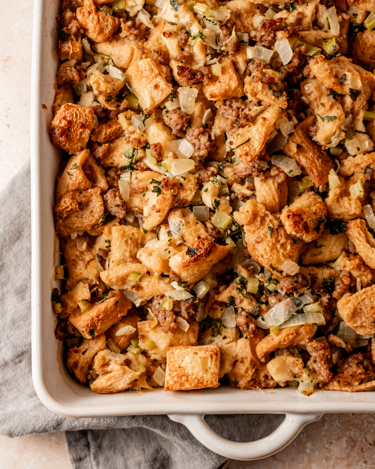 Close-up of the finished sausage and sage stuffing in the casserole dish, baked to a golden brown and garnished with fresh parsley.