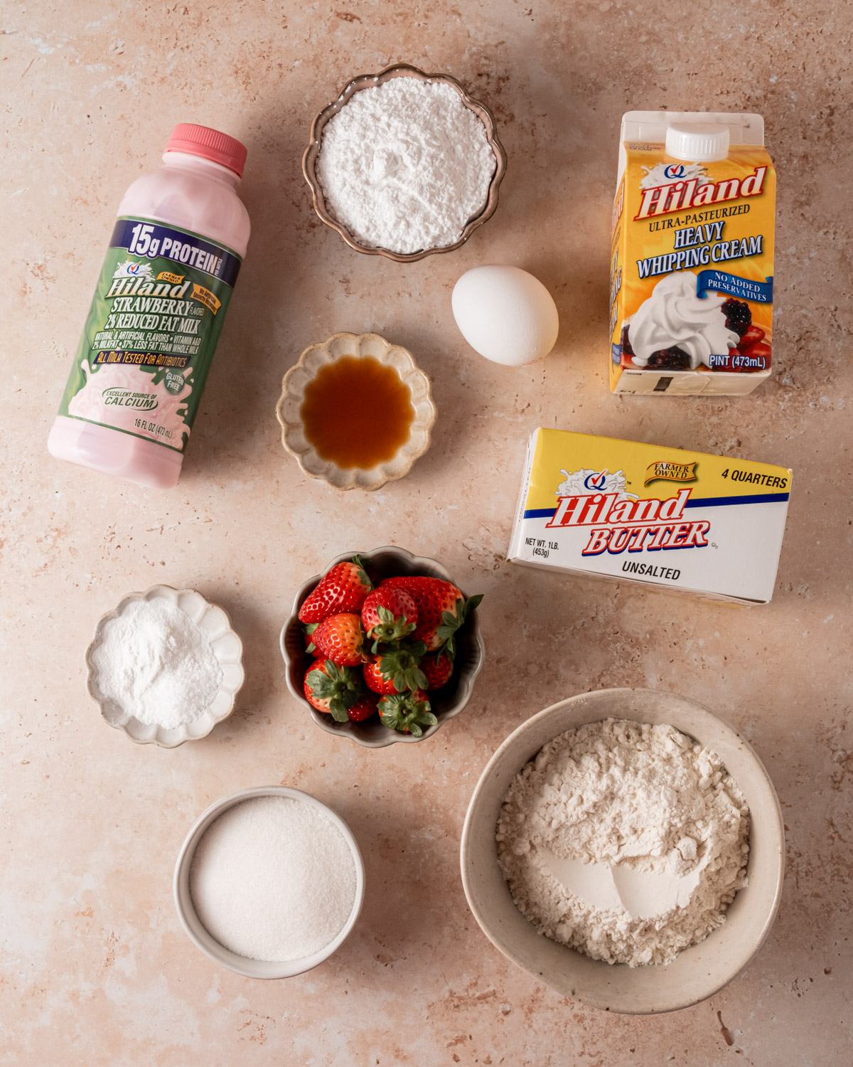 An assortment of ingredients for making strawberry scones, including fresh strawberries, flour, sugar, baking powder, vanilla extract, an egg, butter, and dairy products such as heavy whipping cream and strawberry milk.