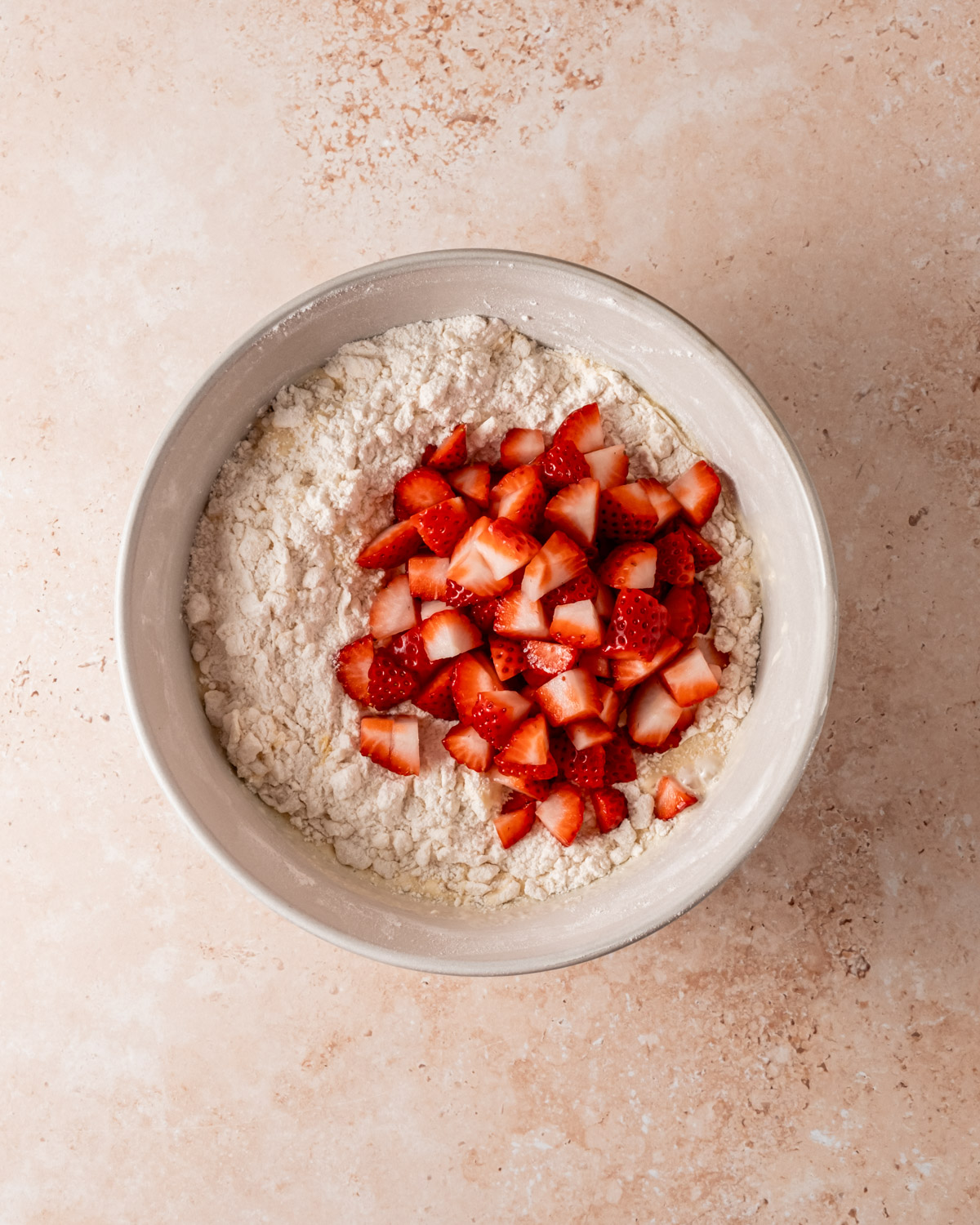 A bowl of flour with freshly chopped strawberries on top, ready to be mixed into the dough.