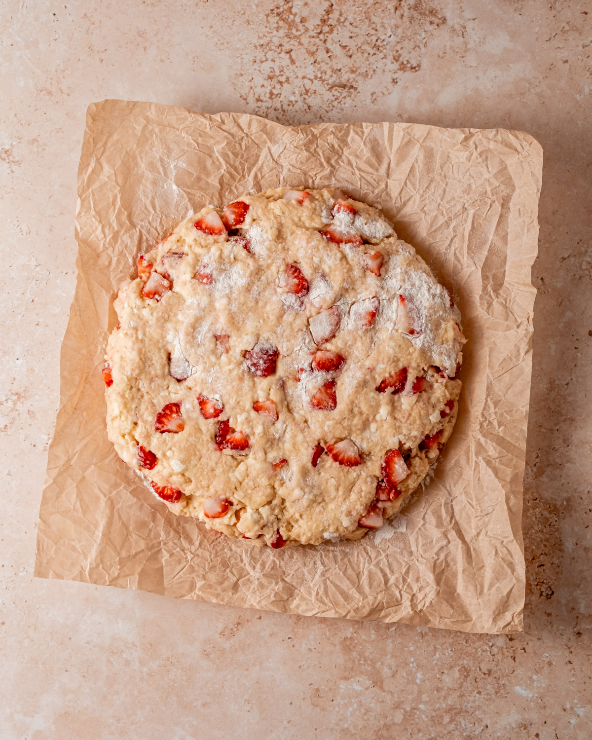 A round, uncooked scone dough with visible chunks of strawberries, resting on parchment paper.