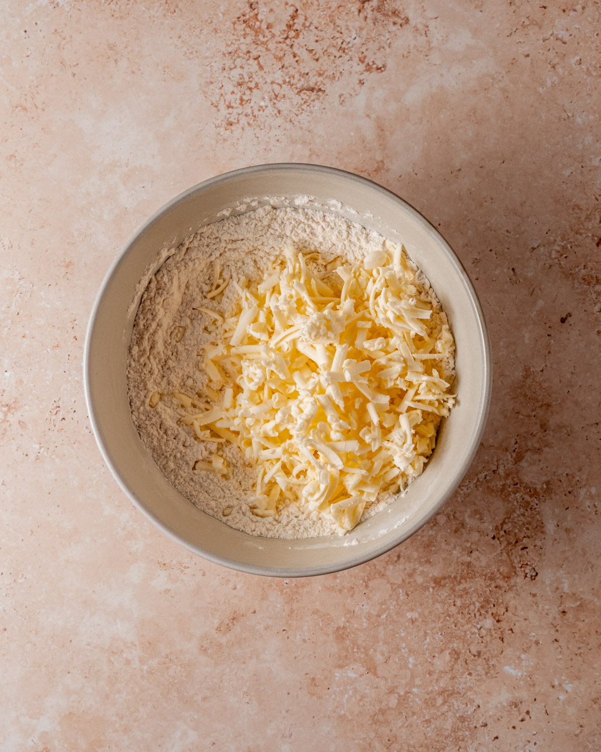 A mixing bowl with flour and grated butter, ready to be combined into scone dough.