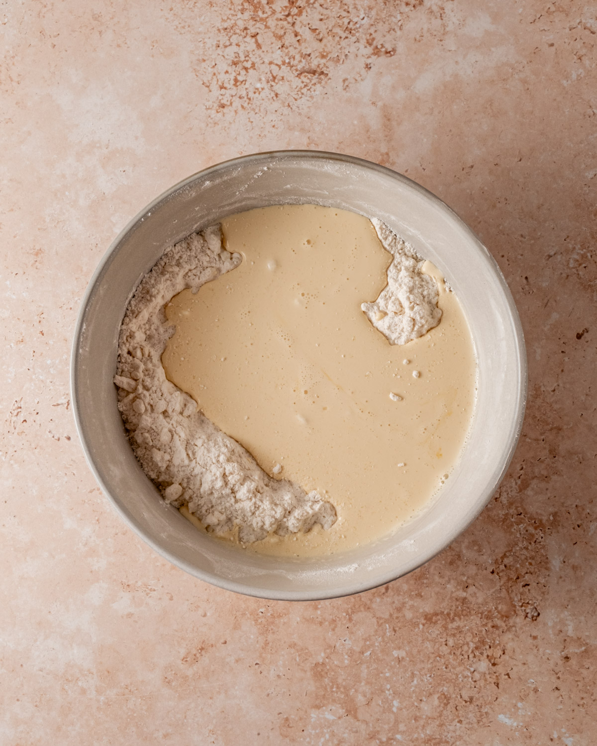 A mixing bowl with flour and a creamy wet ingredient mixture being incorporated, showing the scone dough in progress.