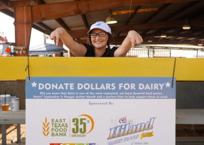Smiling woman pointing at a sign that says "Donate dollars for dairy"