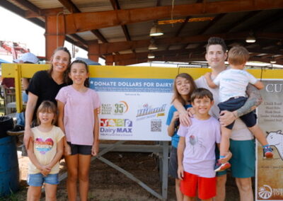 Group of happy adults and kids gathered around a sign that reads "Donate Dollars for Dairy"
